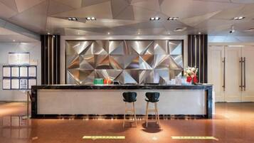 A modern reception area with a geometric wall design, a reception desk, two bar stools, and a polished floor.