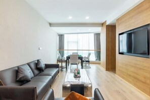 A modern living room with a sofa, coffee table, TV, and dining area.