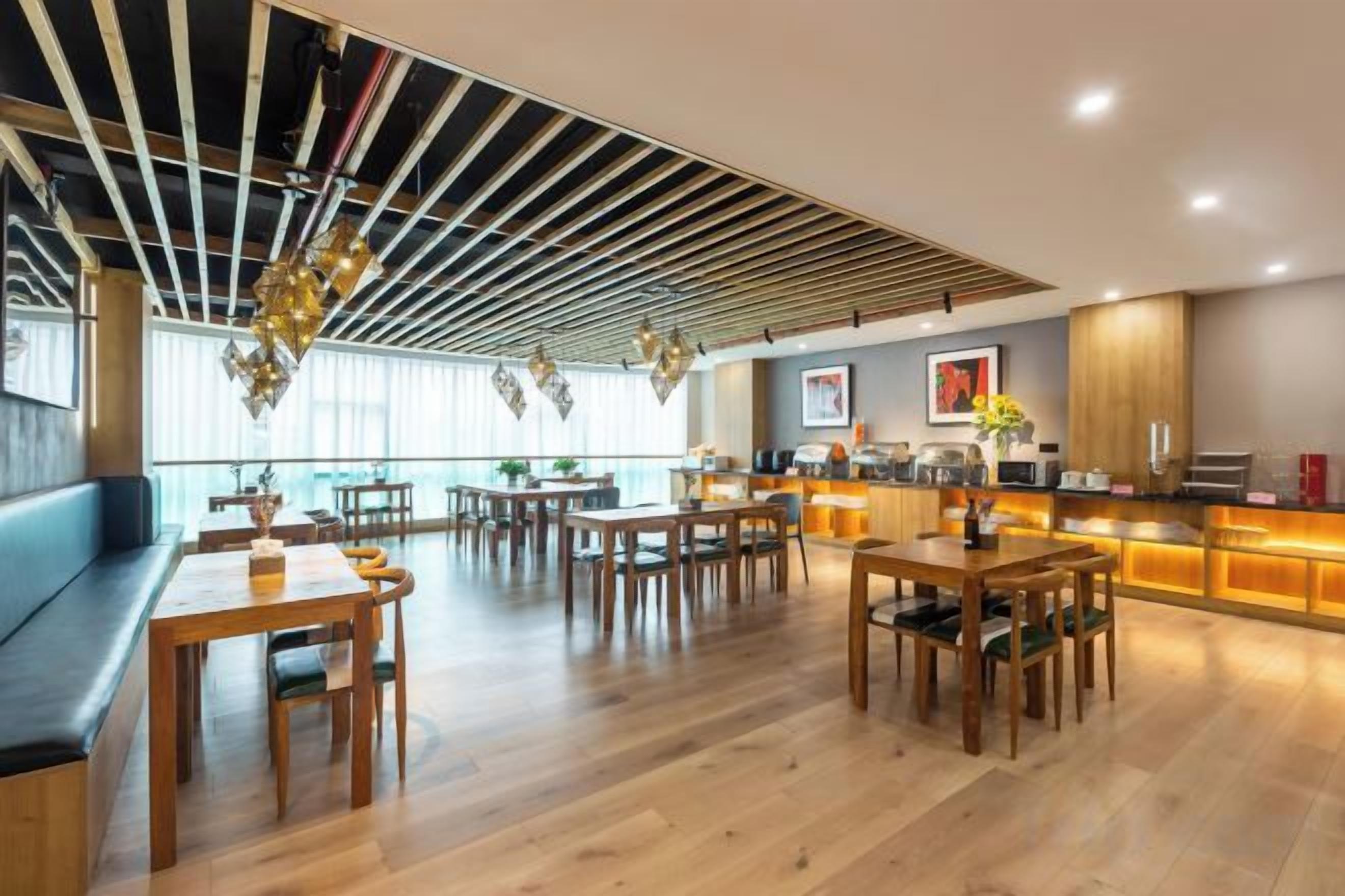 A modern dining area with wooden tables and benches, a bar area with a counter, and a view of the city through large windows.