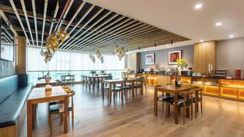 A modern dining area with wooden tables and benches, a bar area with a counter, and a view of the city through large windows.