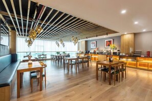 A modern dining area with wooden tables and benches, a bar area with a counter, and a view of the city through large windows. - Tongnan Hotel (Chongqing)