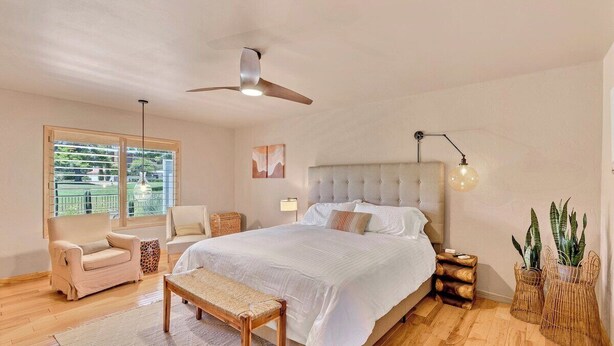 Quarto com uma cama grande, um ventilador de teto, janela com vista, mesa de cabeceira e um banco.
