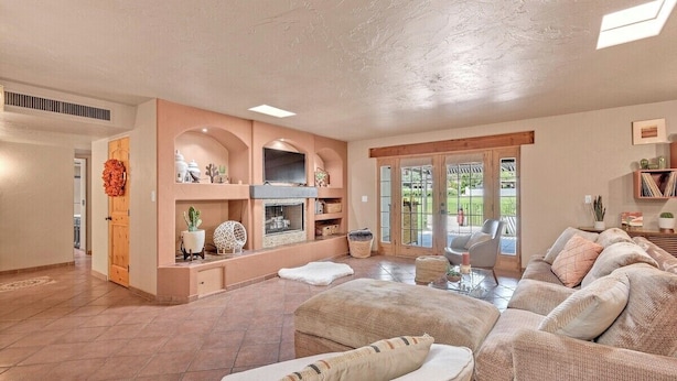 A spacious living room with a fireplace, comfortable seating, and a view through glass doors to an outdoor area.