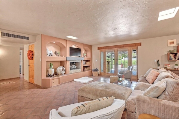 A spacious living room with a fireplace, comfortable seating, and a view through glass doors to an outdoor area.