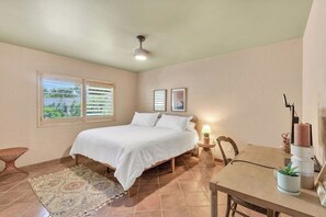 A bedroom with a bed, a nightstand, a lamp, a chair, a table, and a window with blinds. - Dorado Golf Villa,Pet Friendly (Tucson)