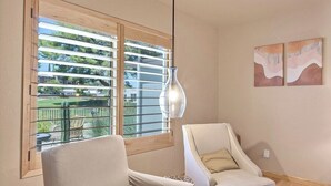 Quarto com duas poltronas, luminária pendente e janela com persianas.