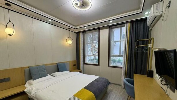 Ein Hotelzimmer mit Bett, Nachttisch, Sessel, Fernseher und Fenstern.