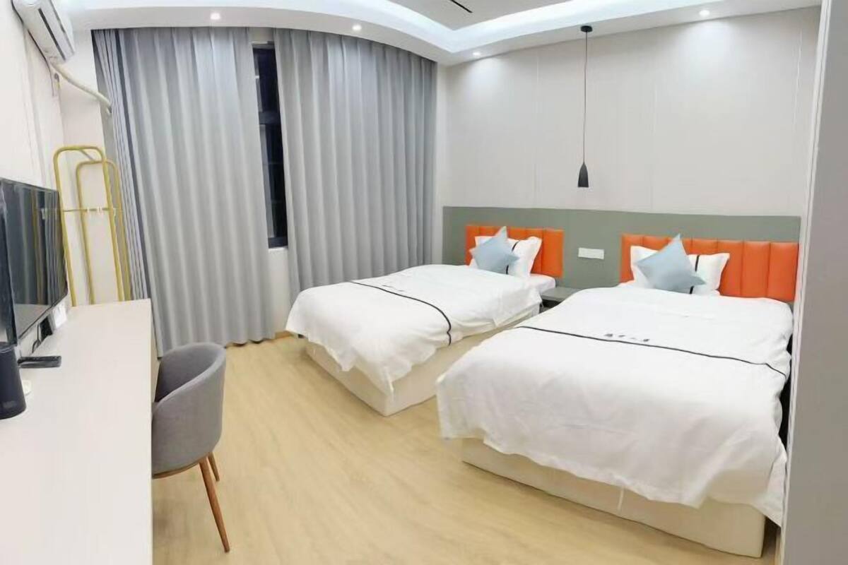 A hotel room with two beds, a desk, a chair, and a TV.