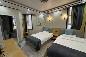 A hotel room with two beds, a desk, a chair, and a wardrobe.