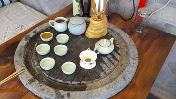 A traditional tea set on a stone tray with multiple cups and a teapot, accompanied by a kettle and a wooden container with chopsticks.