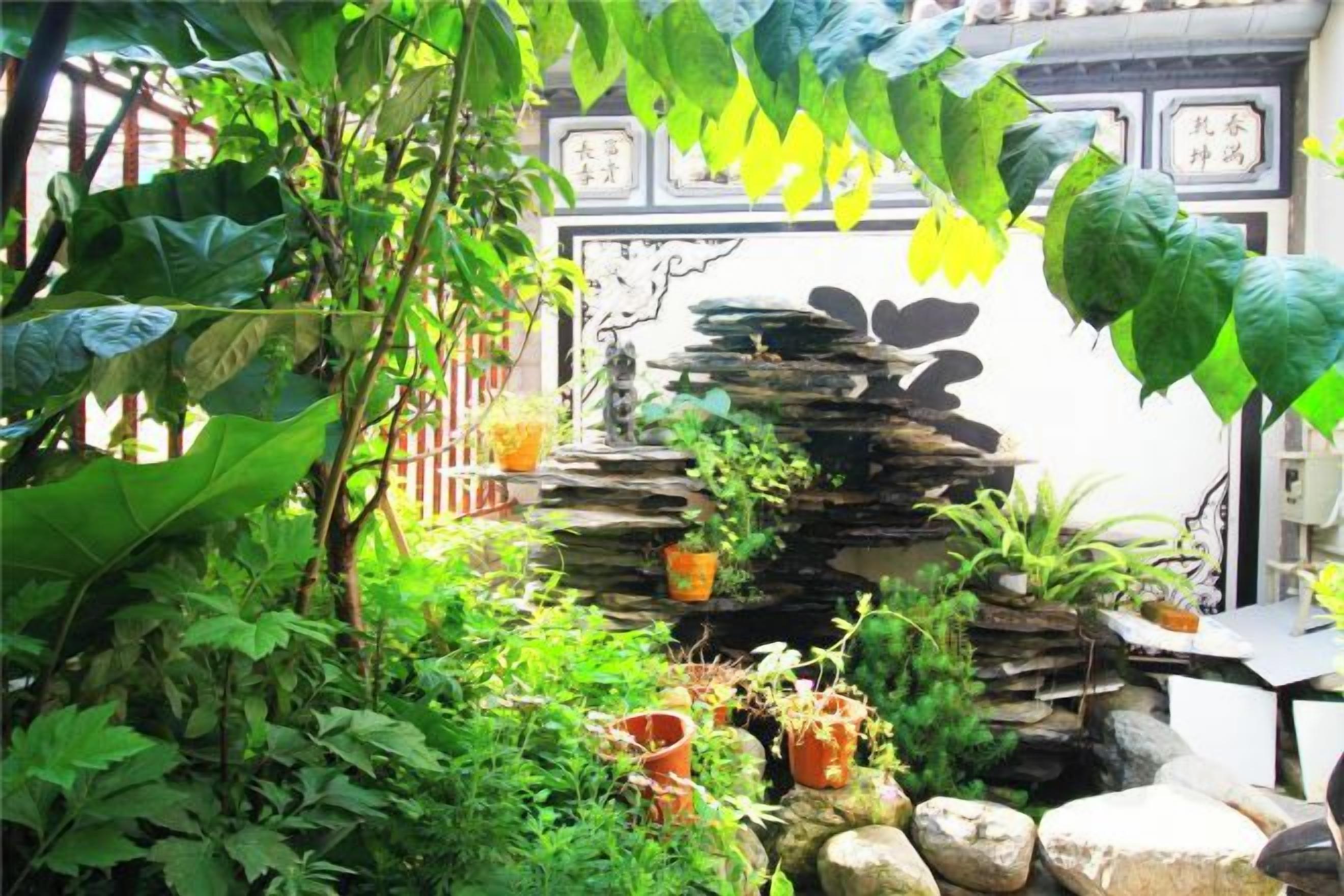 A lush garden with a rock waterfall, potted plants, and a traditional Chinese gate.