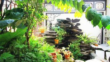 A lush garden with a rock waterfall, potted plants, and a traditional Chinese gate.