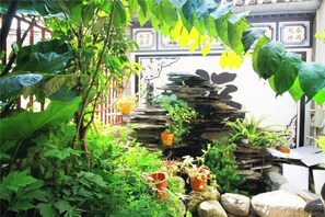 Un exuberante jardín con cascada de piedra, plantas en macetas y una puerta tradicional china.