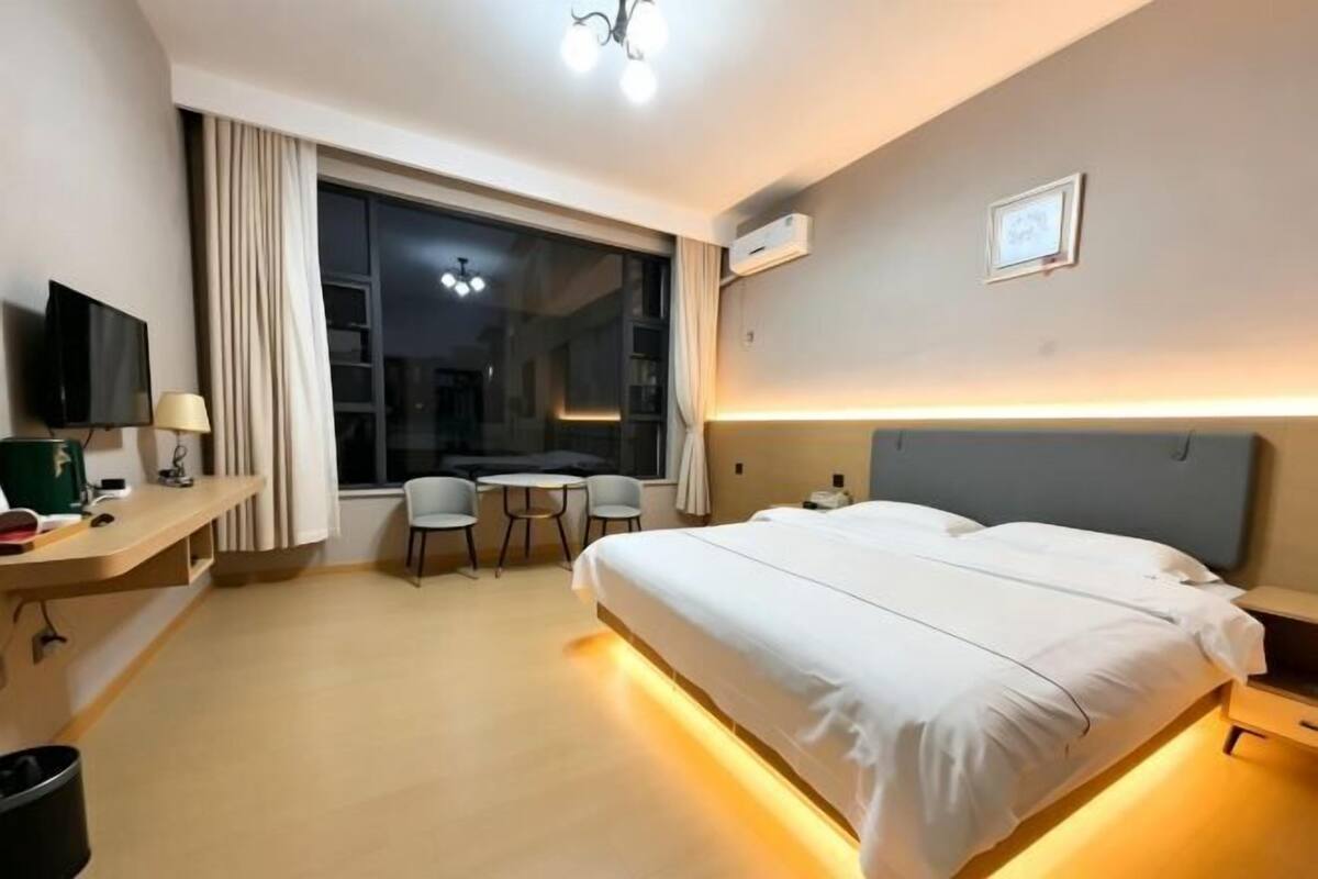 A hotel room with a bed, a desk with a chair, a television, and a large window.