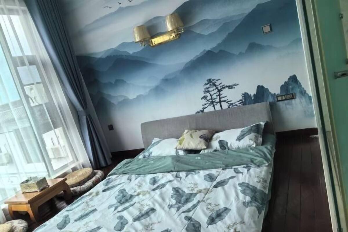 A bedroom with a mountain-themed mural, a bed with a floral bedspread, and a window with curtains.