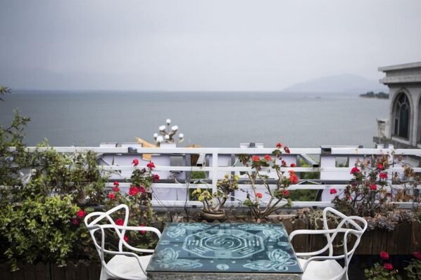 Un espacio al aire libre con mesa y sillas, con vista a un cuerpo de agua y un paisaje montañoso.