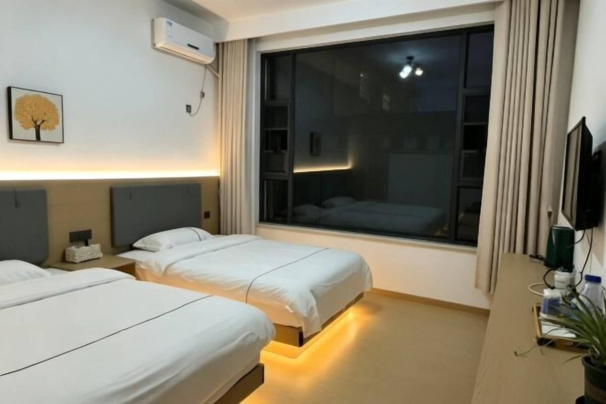 A hotel room with two beds, a large window, a TV, and a desk with a plant.