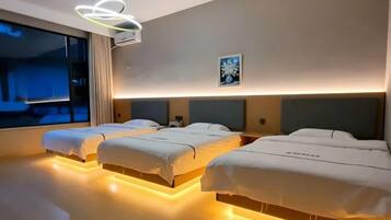 A hotel room with three beds, a large window, and a modern ceiling light fixture.