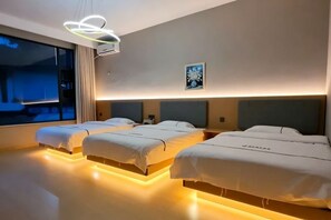 Habitación de hotel con tres camas, un ventanal amplio y un moderno aplique de techo.