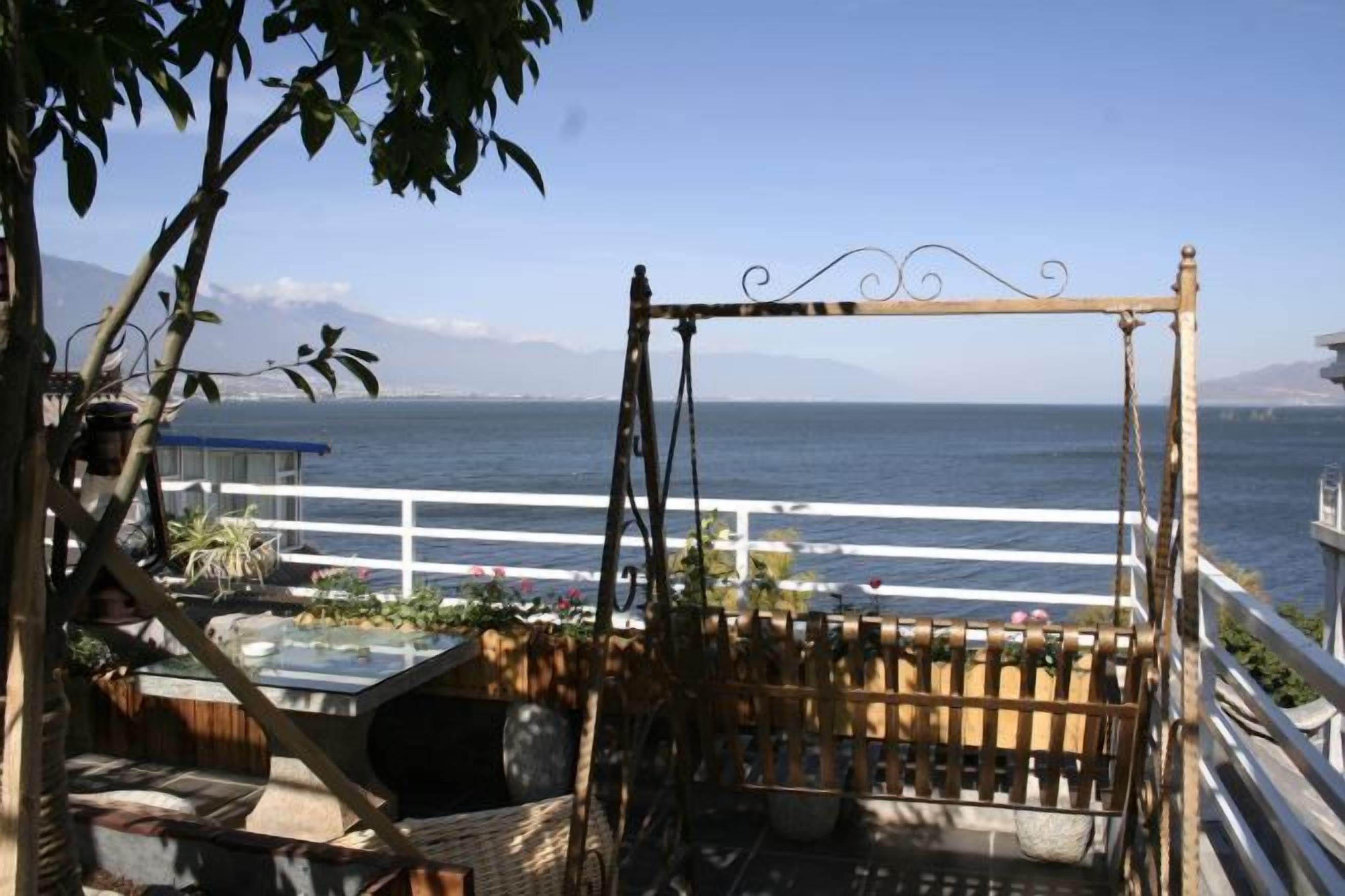 En balkon med udsigt over havet, et gyngestativ og et hvidt gelænder.