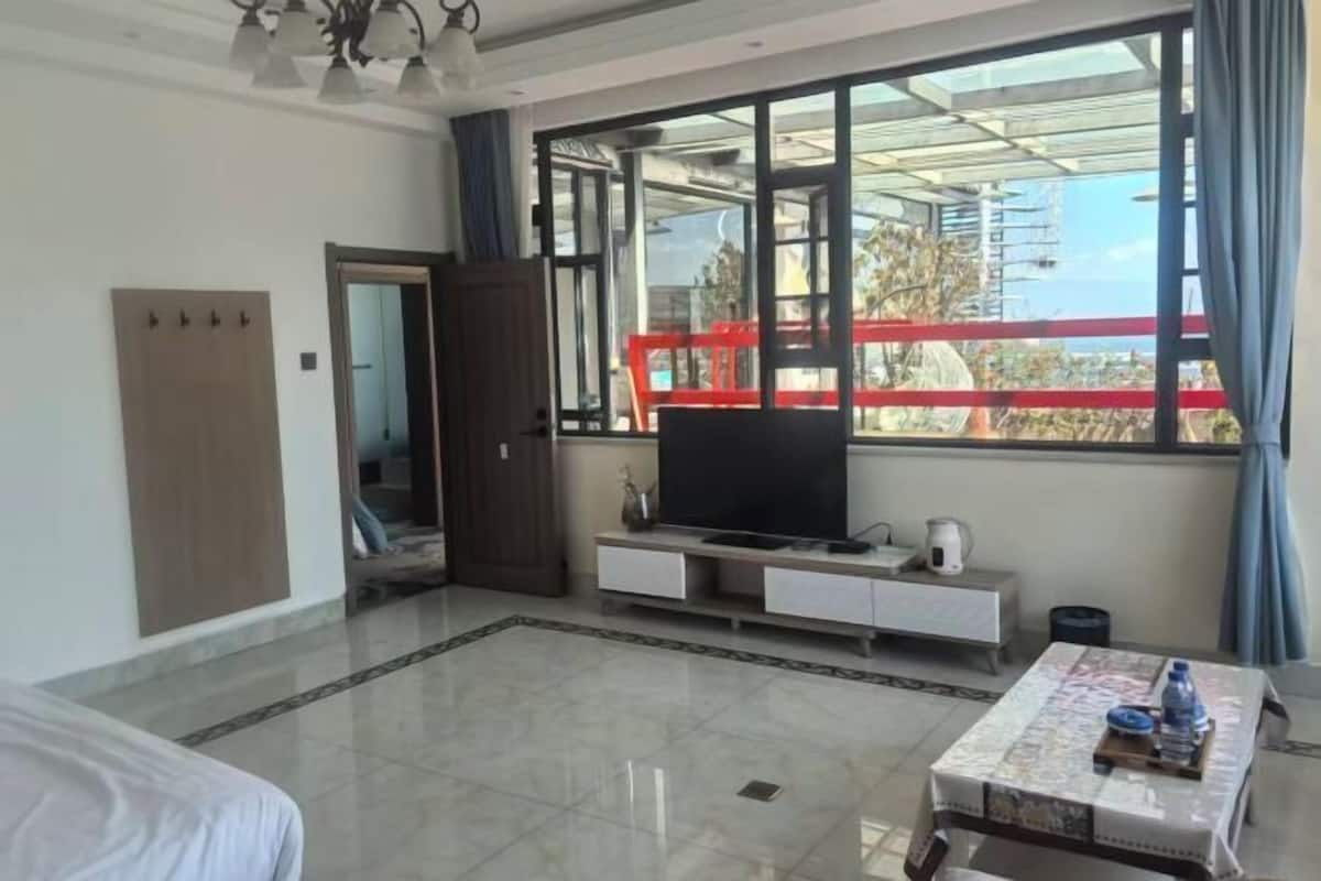 A hotel room with a large window, a bed, a TV on a stand, a small table, and a wardrobe.