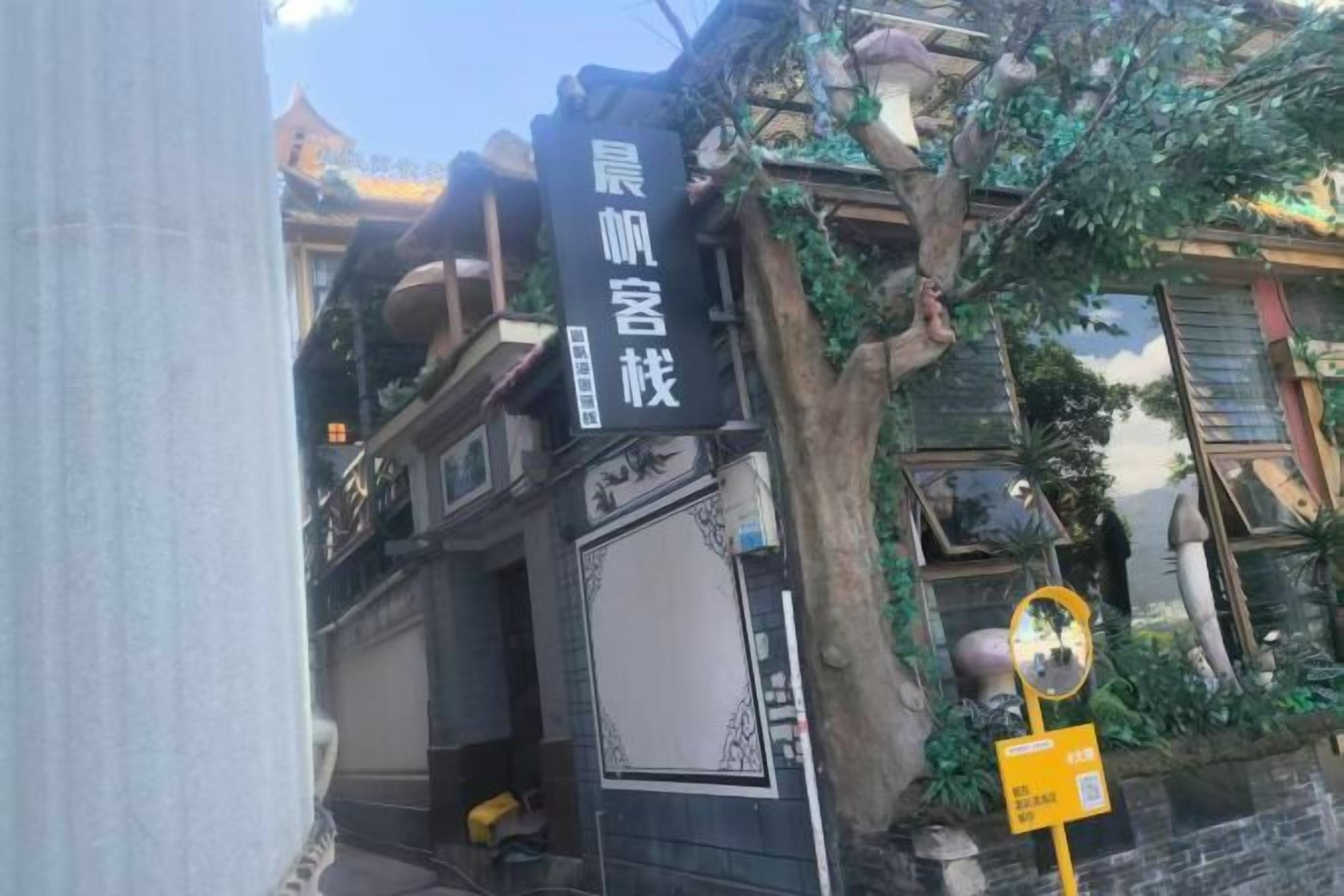 A traditional building with a black facade, a signboard with Chinese characters, and a tree with hanging plants.