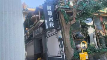A traditional building with a black facade, a signboard with Chinese characters, and a tree with hanging plants.