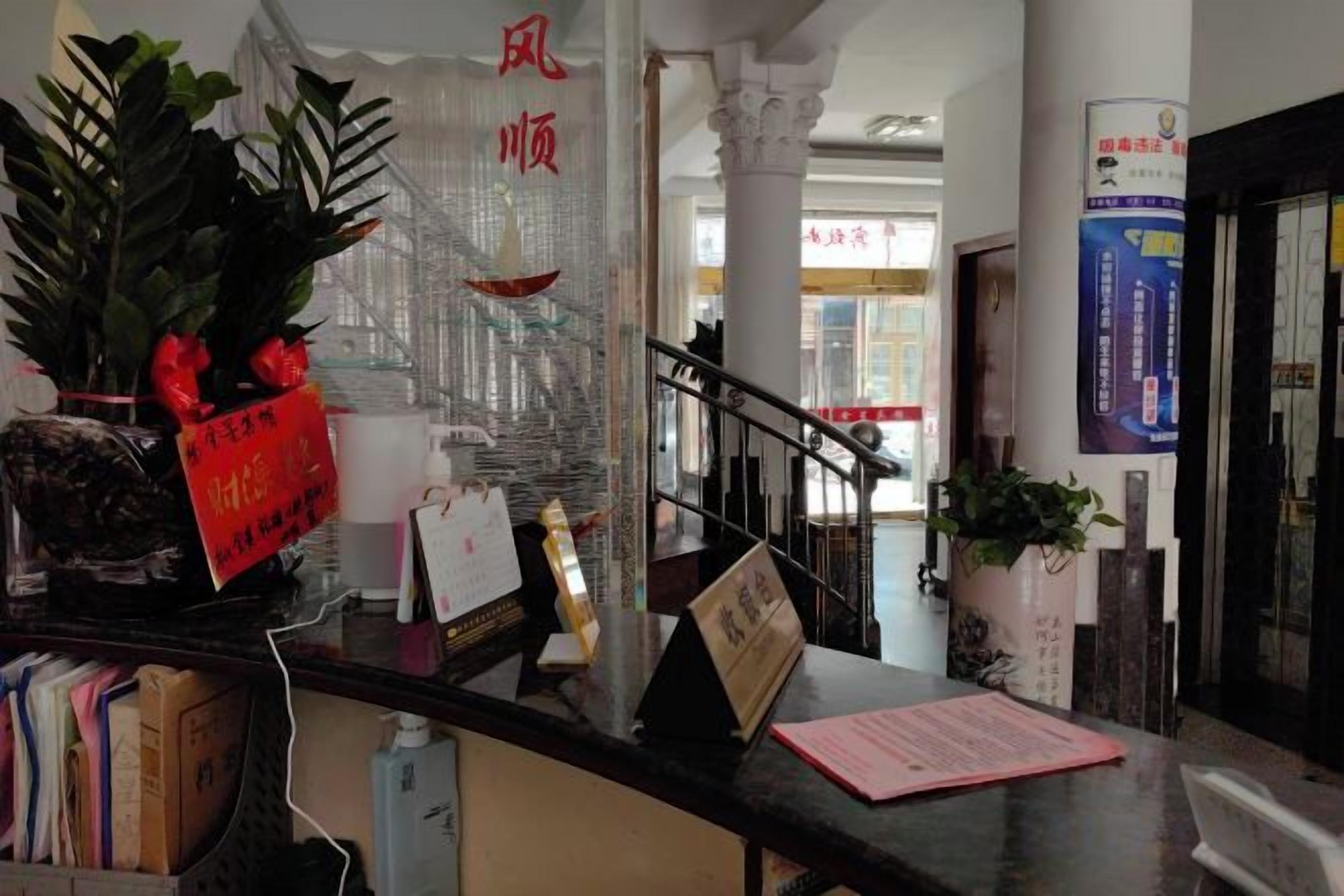 A reception desk with a potted plant, a red sign, and a staircase in the background.