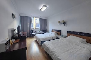 Habitación de hotel con dos camas, un escritorio, una silla, un televisor y una ventana con cortinas.