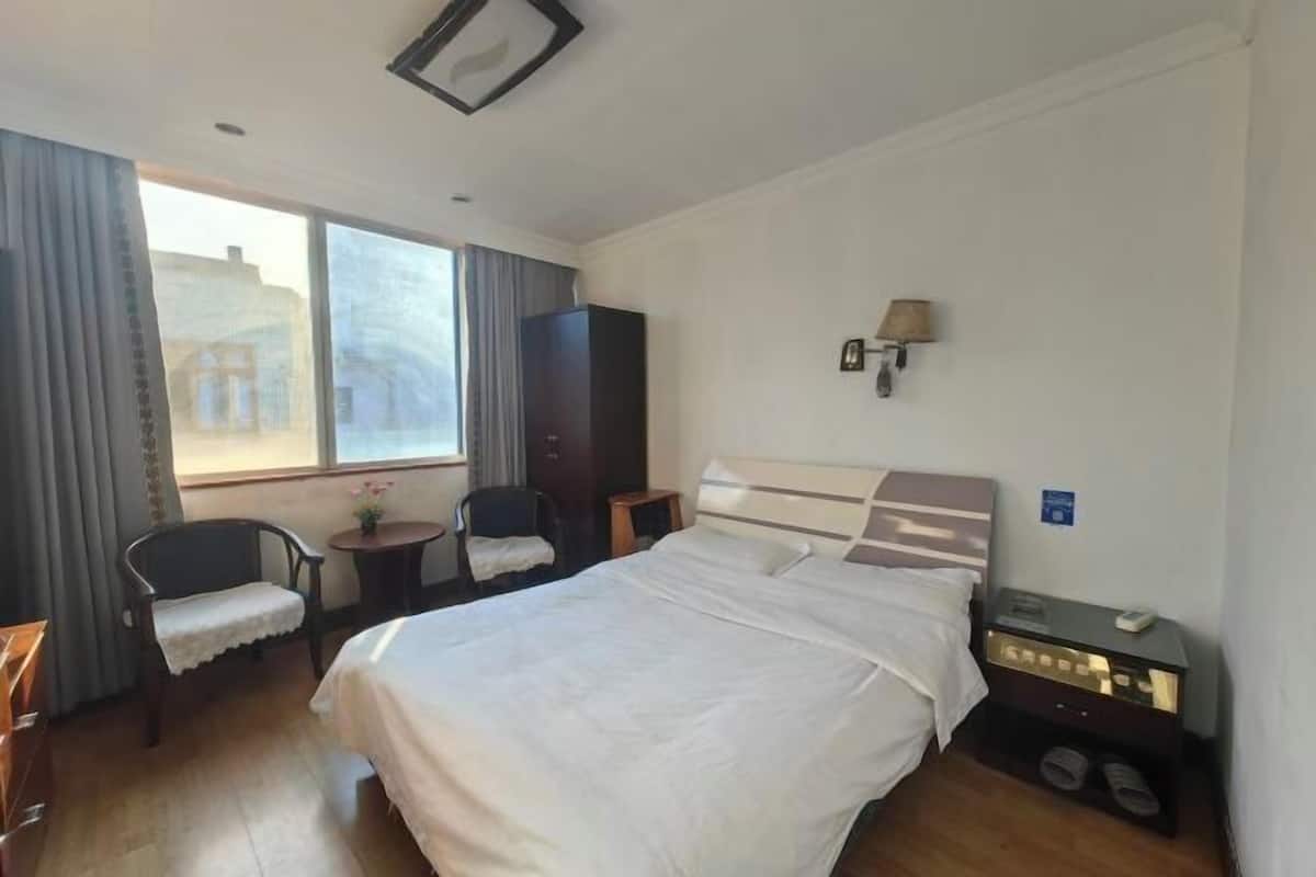 Ein Hotelzimmer mit einem großen Bett, einem Schreibtisch, einem Stuhl, einem kleinen Tisch und einem Fenster mit Vorhängen.