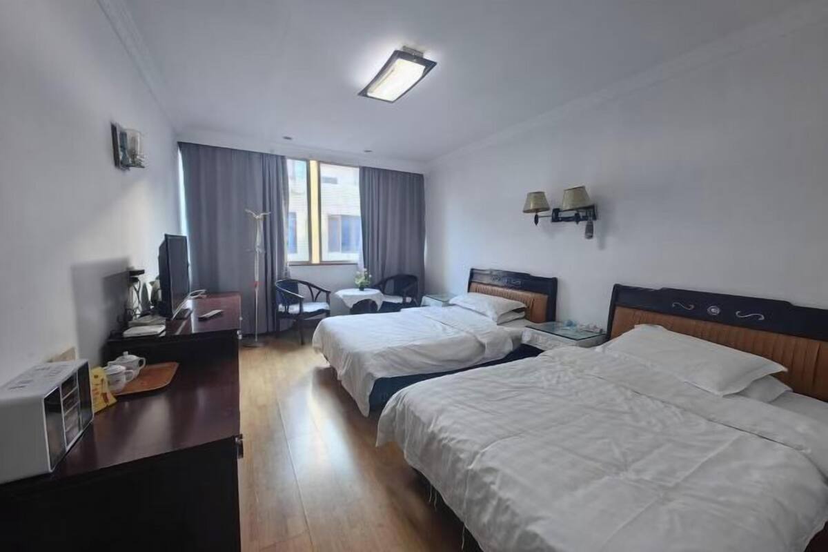 Ein Hotelzimmer mit zwei Betten, einem Schreibtisch, einem Sessel, einem Fernseher und einem Fenster mit Vorhängen.