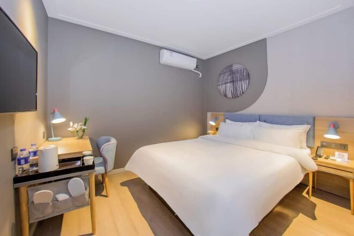 A hotel room with a bed, bedside tables, a desk with a chair, a small seating area, and a TV.