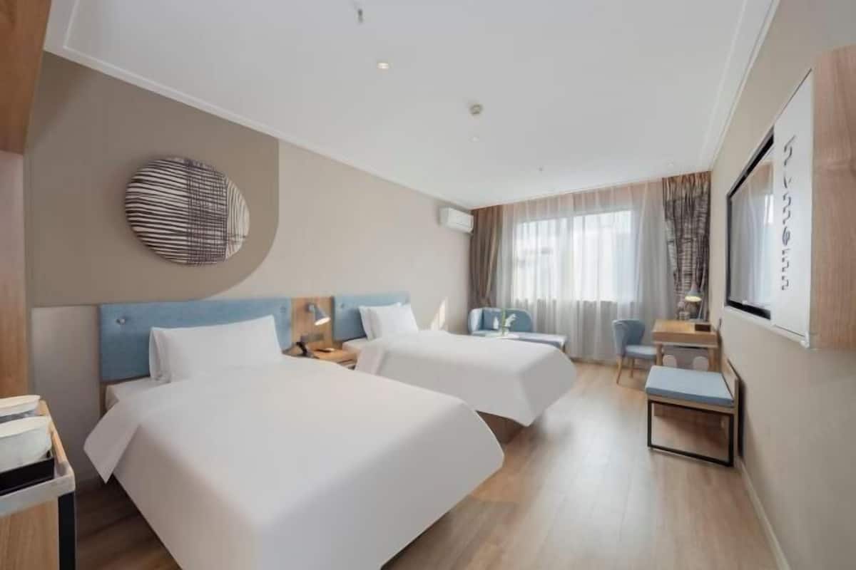 A hotel room with two beds, a desk, a chair, and a small table.