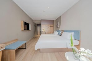 Een moderne hotelkamer met een groot bed, een bankje, een televisie en een tafeltje met een bloemenvaas.