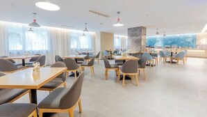 A modern dining area with multiple tables and chairs, large windows with curtains, and pendant lighting.