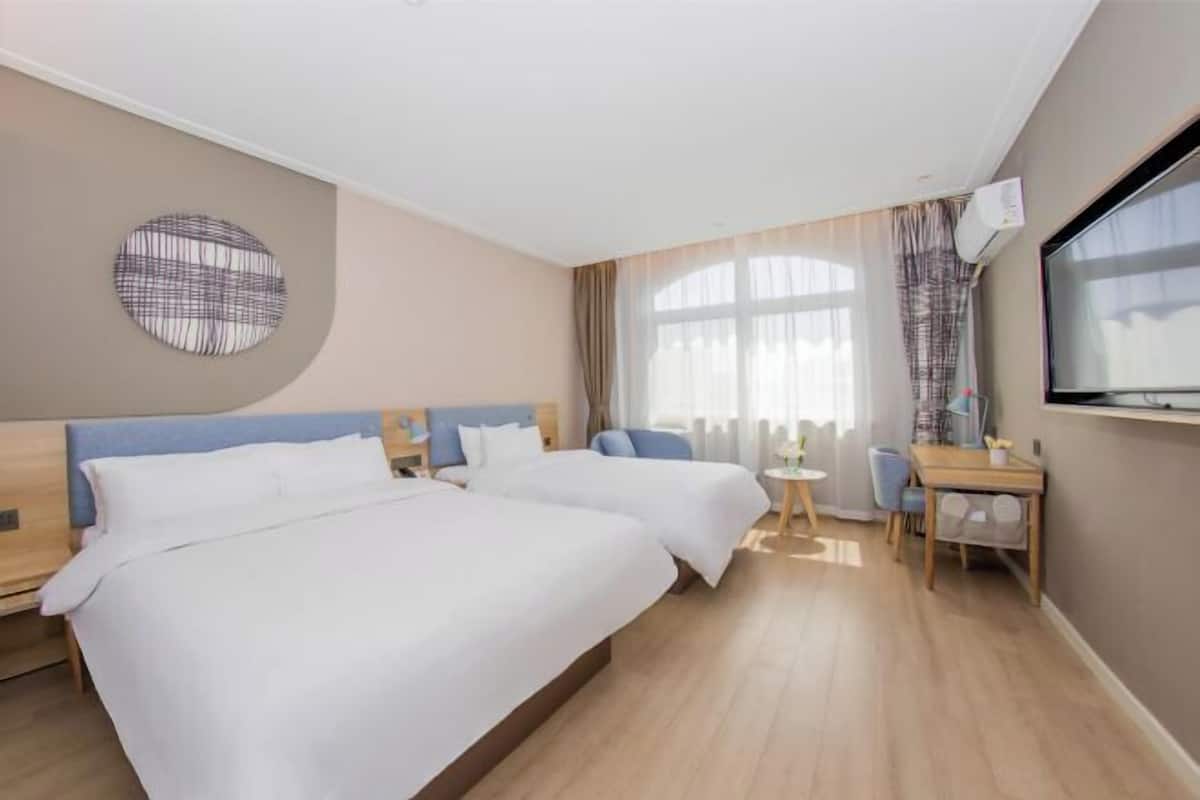 A hotel room with two beds, a small table, a chair, a TV, and a window with curtains.