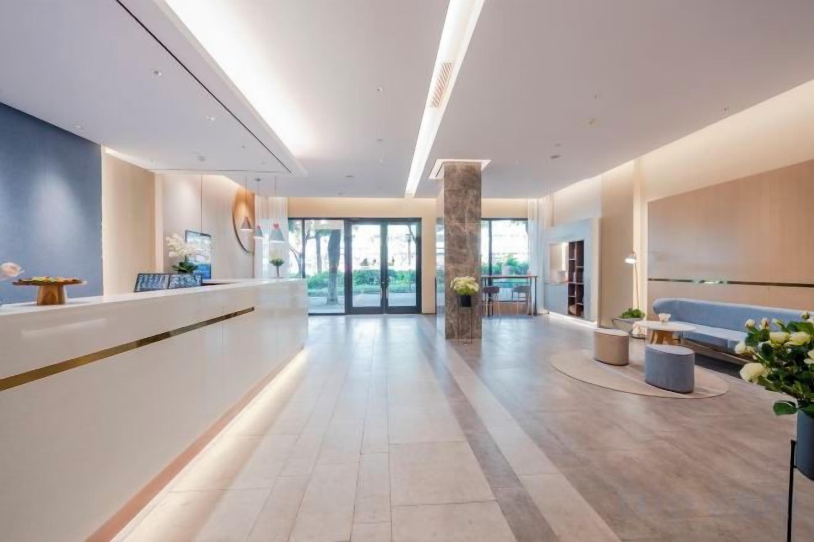 A modern hotel lobby with a reception desk, seating area, and a large window.