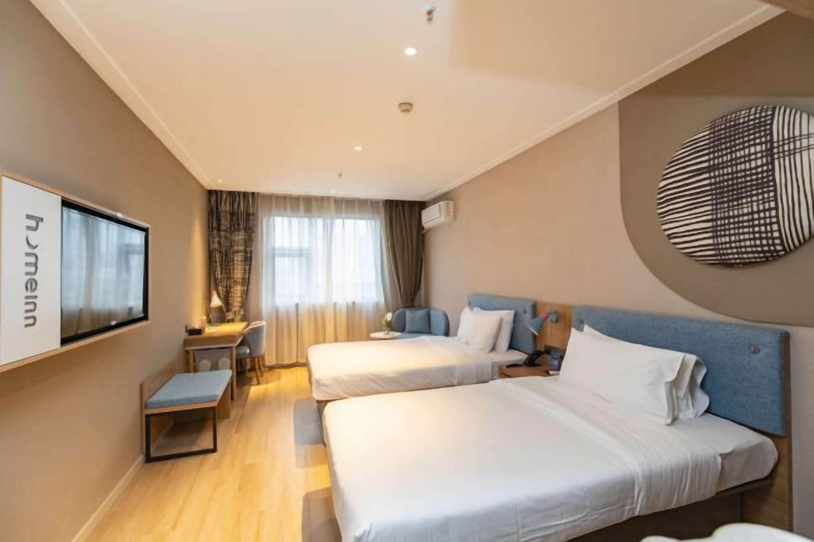 A hotel room with two beds, a desk, a chair, a TV, and a large wall decoration.