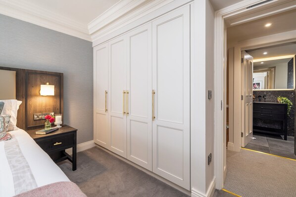 A bedroom with a large white wardrobe, a bedside table with a lamp, and a view into the bathroom.
