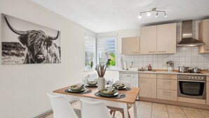 A modern kitchen with light wood cabinets, a stainless steel range hood, and a dining area with a wooden table and white chairs. - Comfortable apartment near Basel with parking space (Weil am Rhein)