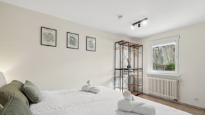 A bedroom with a large bed, two pillows, a radiator, a window with a view, and three framed artworks on the wall. - Comfortable apartment near Basel with parking space (Weil am Rhein)