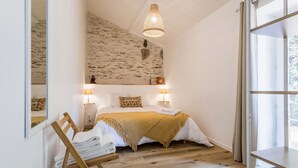 Ein Schlafzimmer mit einem Bett, zwei Nachttischlampen, einem Holzsessel, einem Spiegel und einer Hängeleuchte.