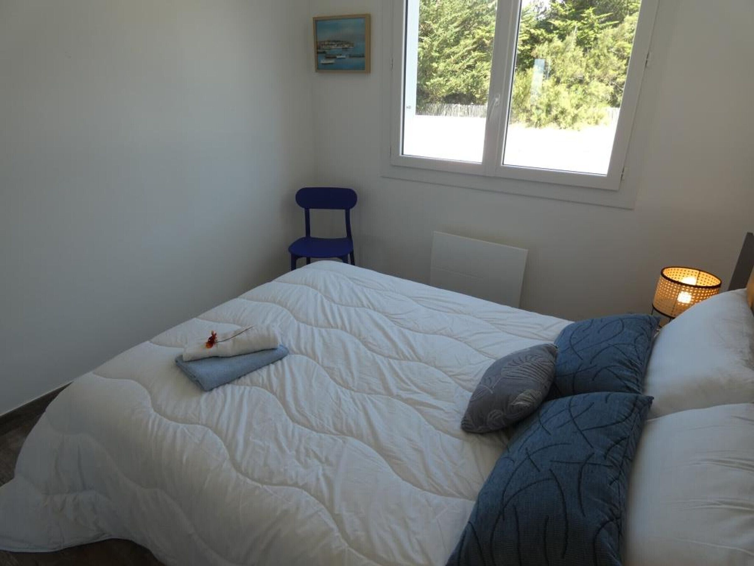 Une chambre à coucher avec un lit, une chaise, une lampe et une fenêtre donnant sur des arbres.