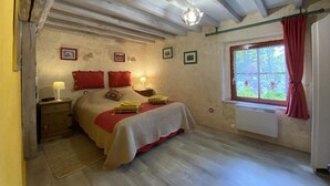 Un dormitorio con cama, mesitas de noche, una ventana con cortinas y una lámpara colgante.