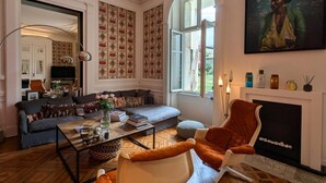 A living room with a sofa, armchair, and coffee table, a fireplace, and a large window. - Apartment with terrace, garden and WIFI in the historic heart of Angoulême (Angoulême)
