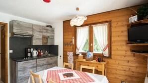 A cozy room with a wooden interior, a dining table with a checkered tablecloth, a kitchen area with modern appliances, and a television on a wooden shelf.