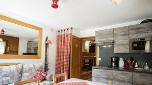 A cozy room with a checkered table, wooden furniture, a bunk bed, and a kitchenette with modern appliances.
