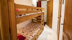 A bunk bed with patterned bedding, a wooden door, and a light fixture on the ceiling.