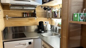 Una cuina compacta amb rentaplats, cafetera, un rentamiques i una campana extractora. Hi ha prestatges amb espècies i una caixa de verbena.