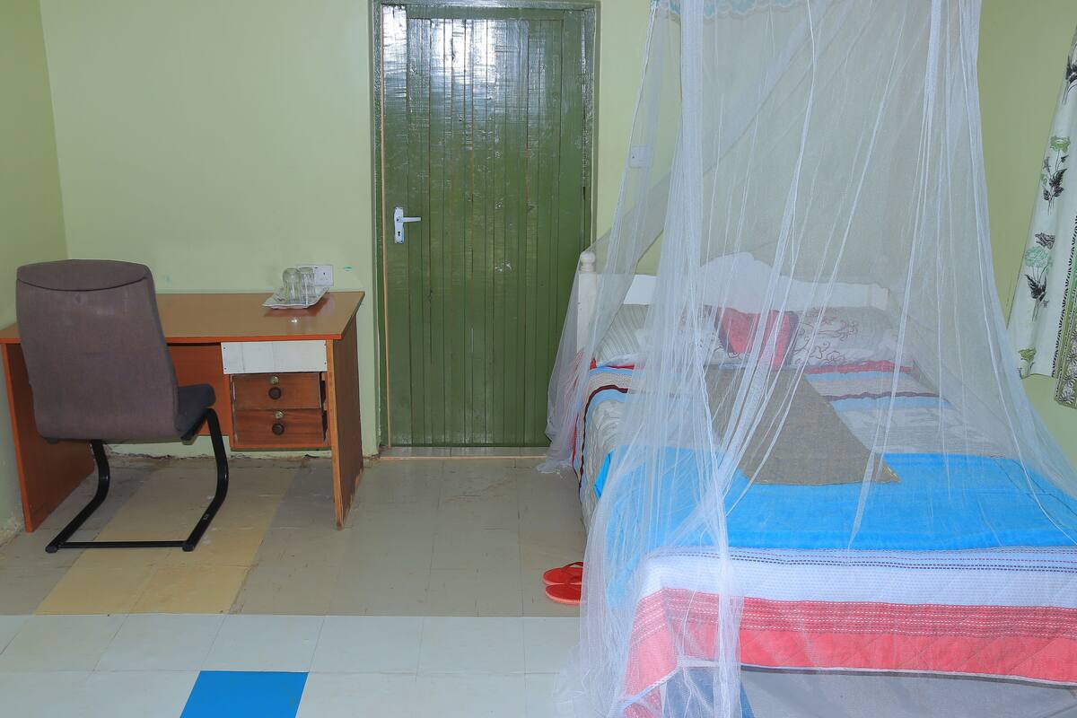 Une chambre avec un lit recouvert d’une moustiquaire, un bureau avec une chaise et une porte verte.